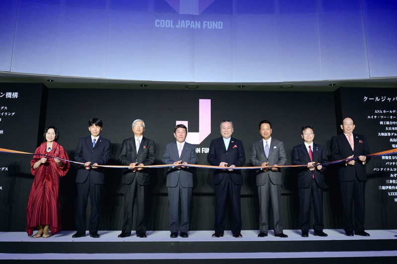 テープカット(左から、松島みどり経産副大臣、山本一太内閣府特命担当相・知的財産戦略本部副本部長、飯島一暢クールジャパン機構会長、 茂木経産相、太田社長、甘利経済再生担当相、世耕弘成内閣官房副長官、槍田松瑩海外需要開拓委員会委員長)
